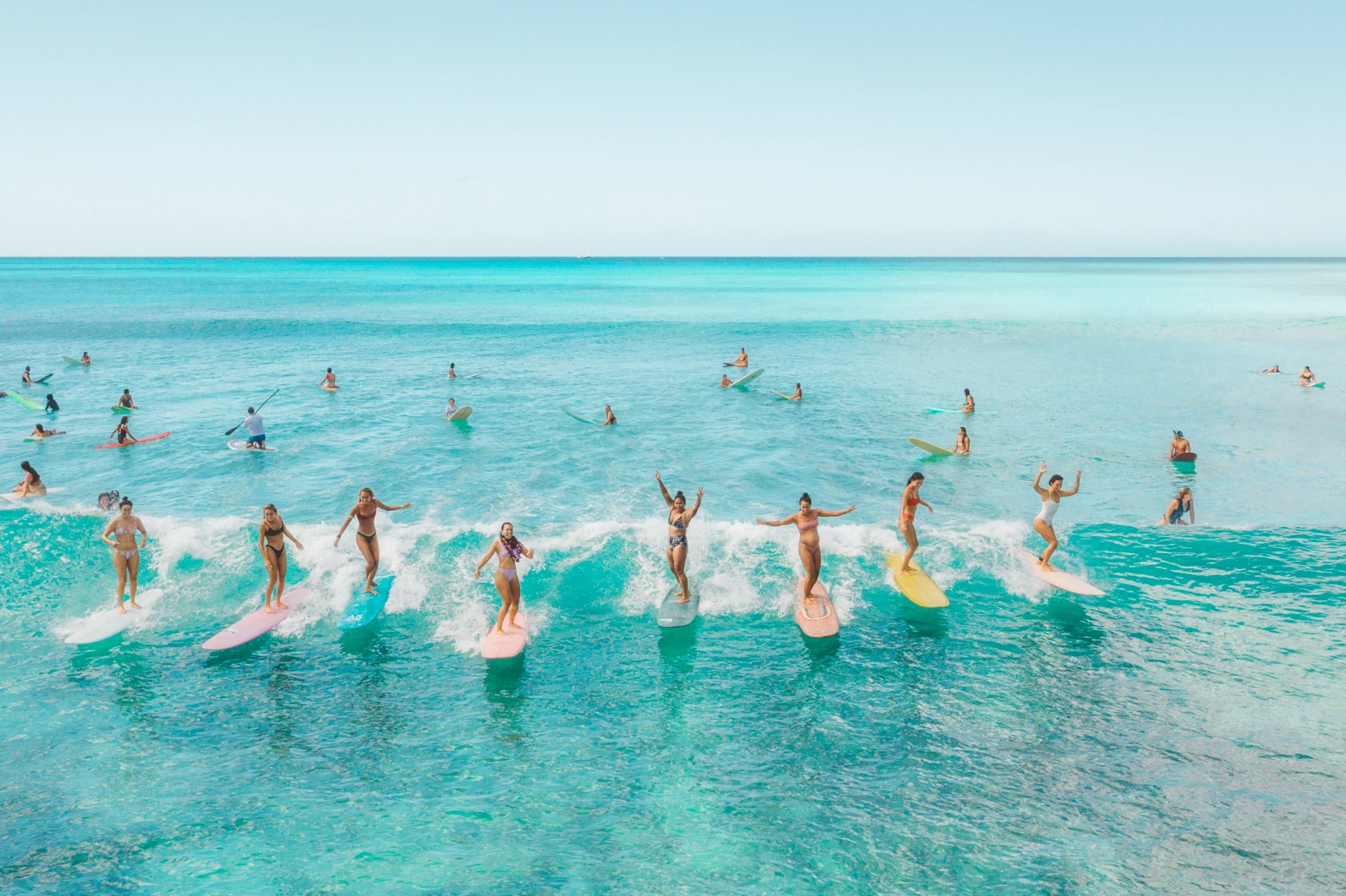 Many surfers aligned in a row as they ride a shallow wave to shore