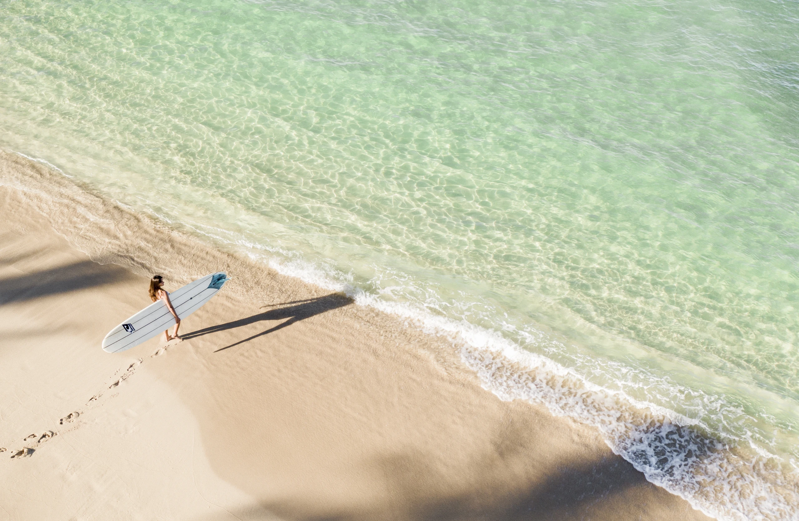 A surfer holding her board underarm walking into the ocean