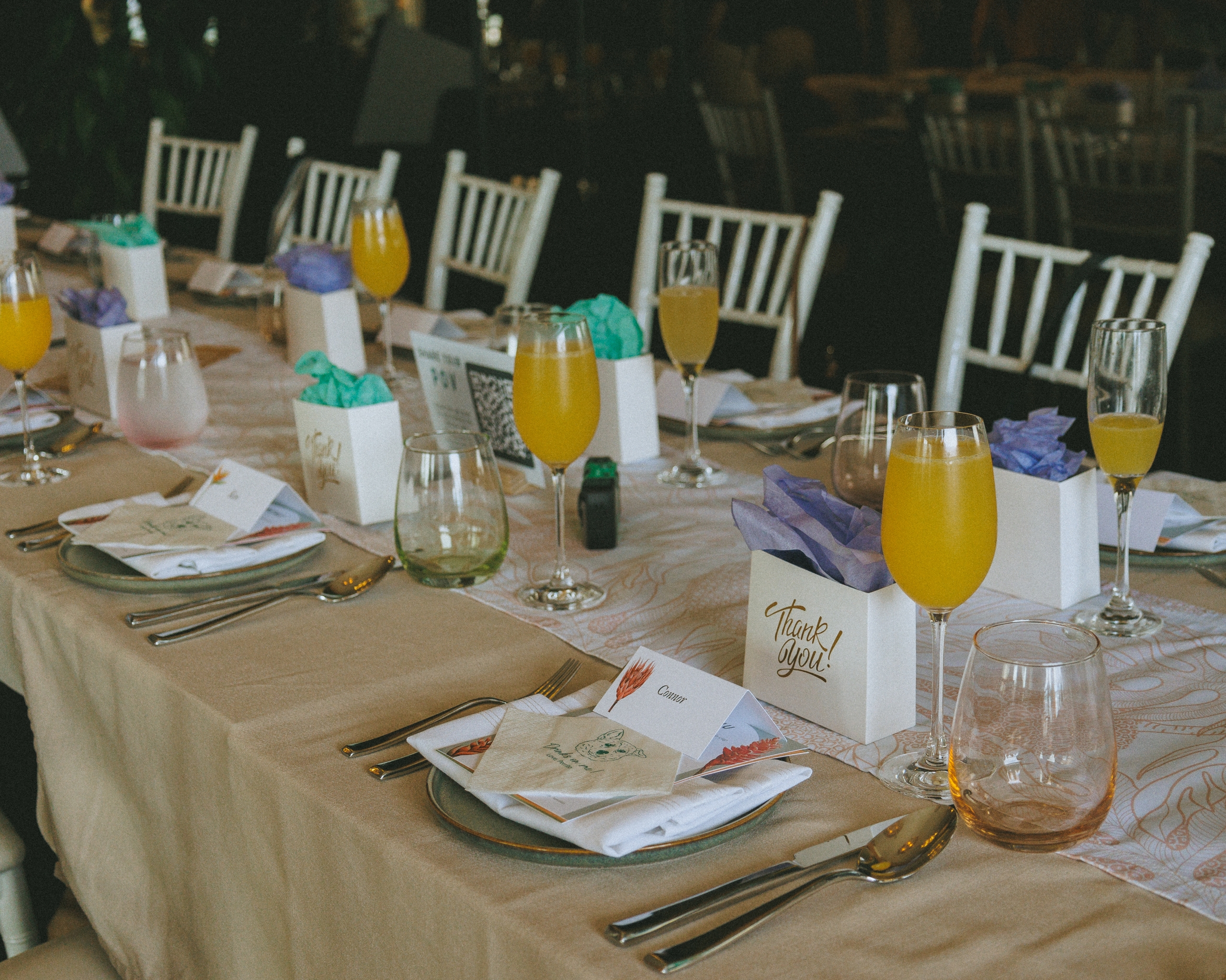 Wedding dinner table set for guests complete with mimosas, custom seating name cards, and gift bags
